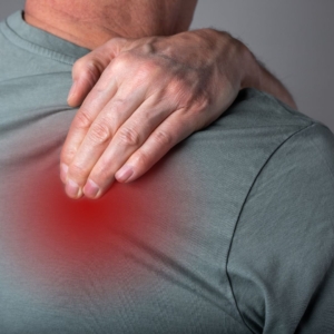 Man in green shirt holding is shoulder in pain