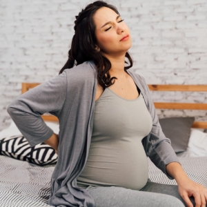 Pregnant woman sitting on a bed holding her back